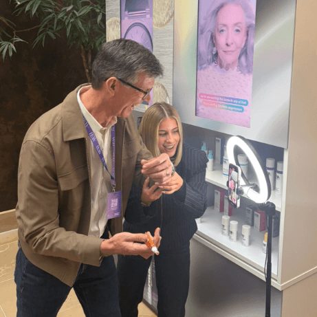 Two teammates trying products at a beauty-brand demo station under a ring light