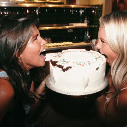 Two teammates biting into opposite sides of a sprinkle-topped cake