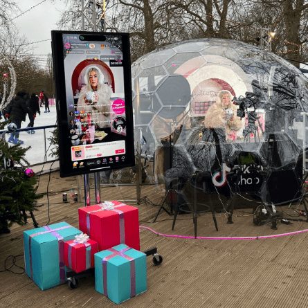 A TikTok Shop LIVE broadcasting from a clear igloo beside an ice rink, presents stacked outside