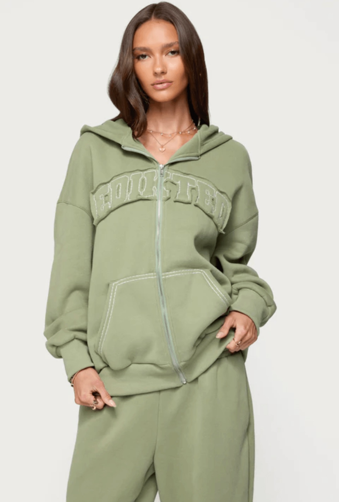 An oversized sage-green Edikted zip hoodie worn by a model, framed from the shoulders down