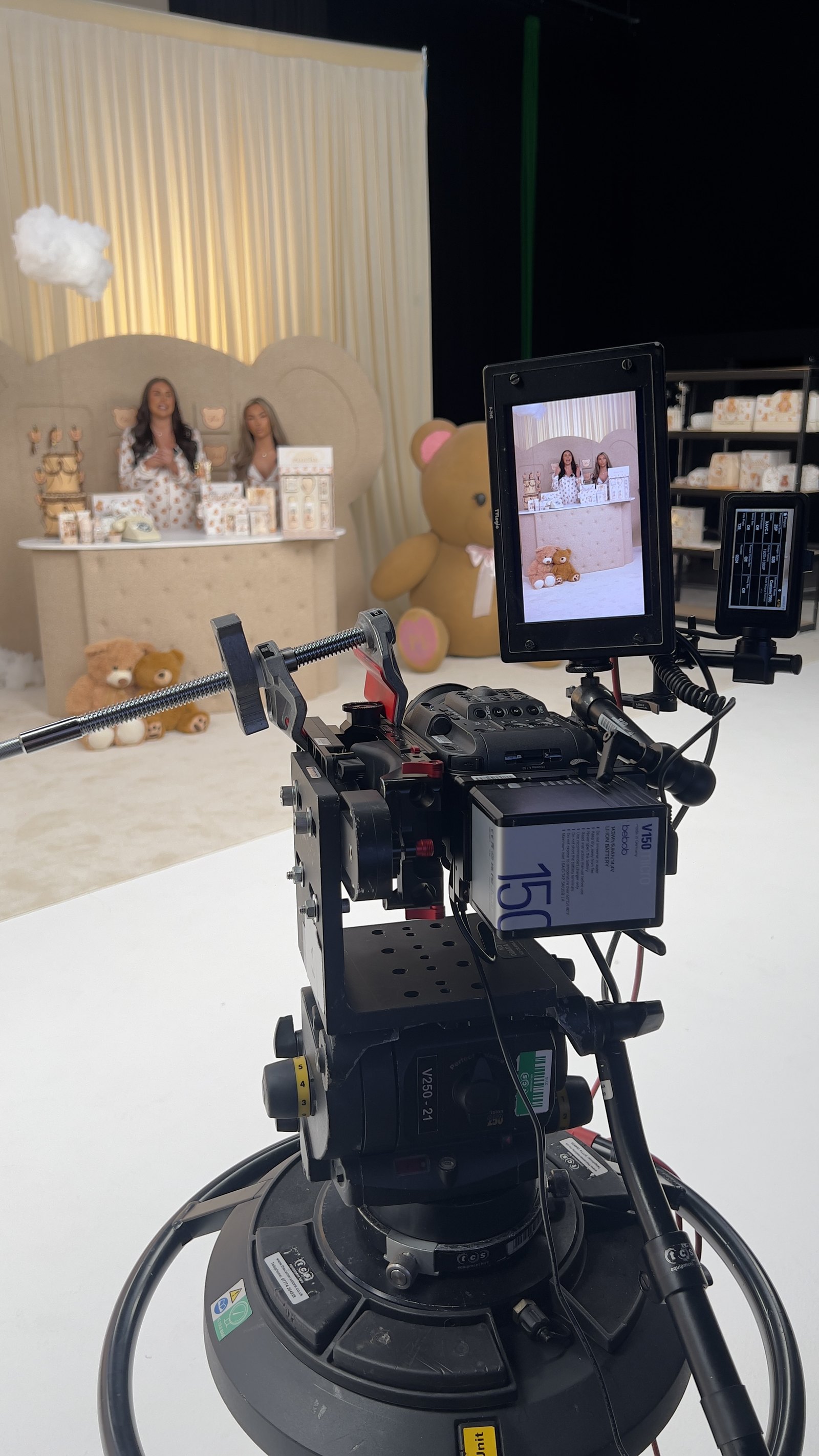 The broadcast camera and monitor framing a two-host LIVE on a dressed set